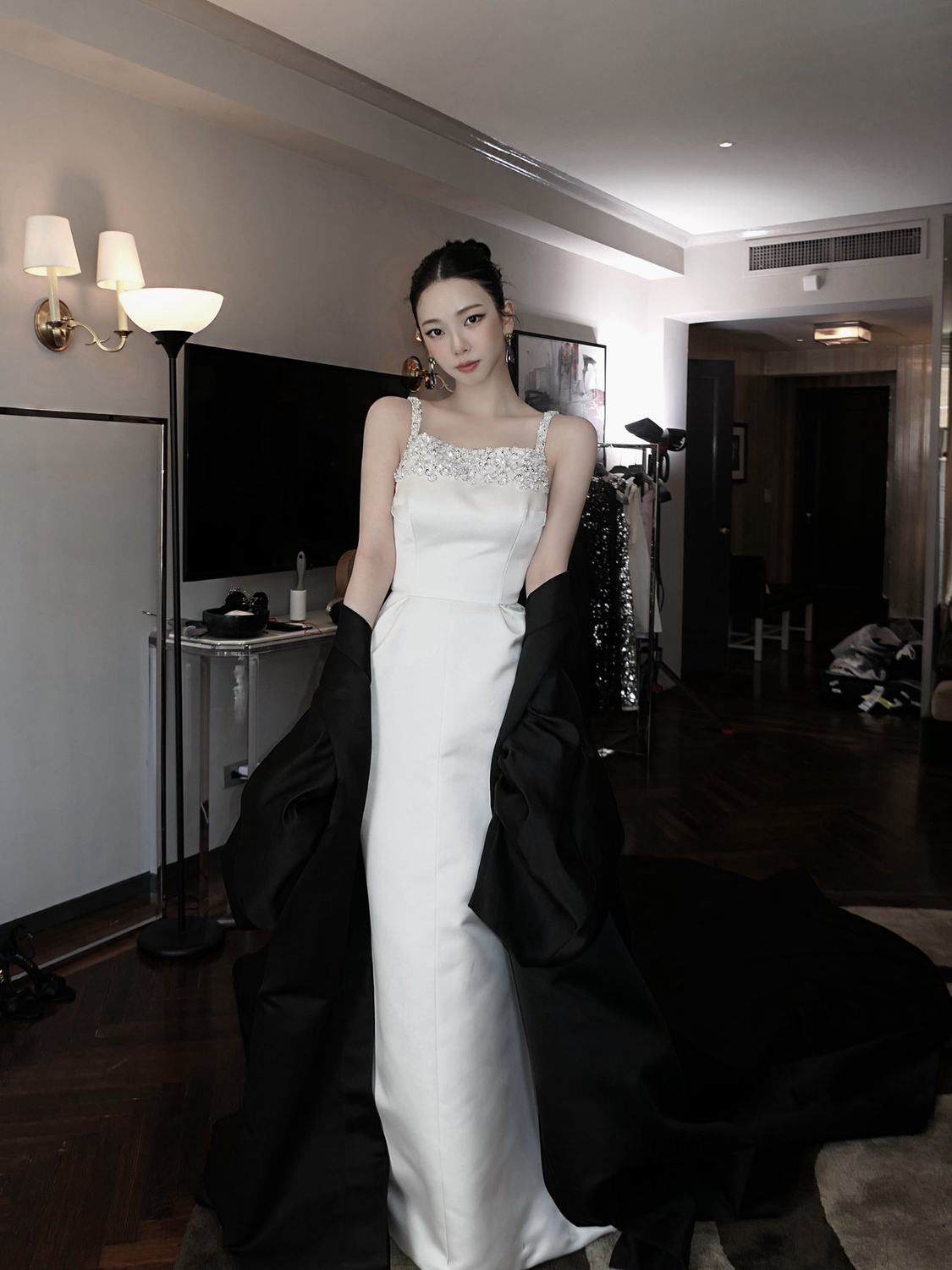 Full-length backstage portrait of Karina in a white Prada gown and black cape