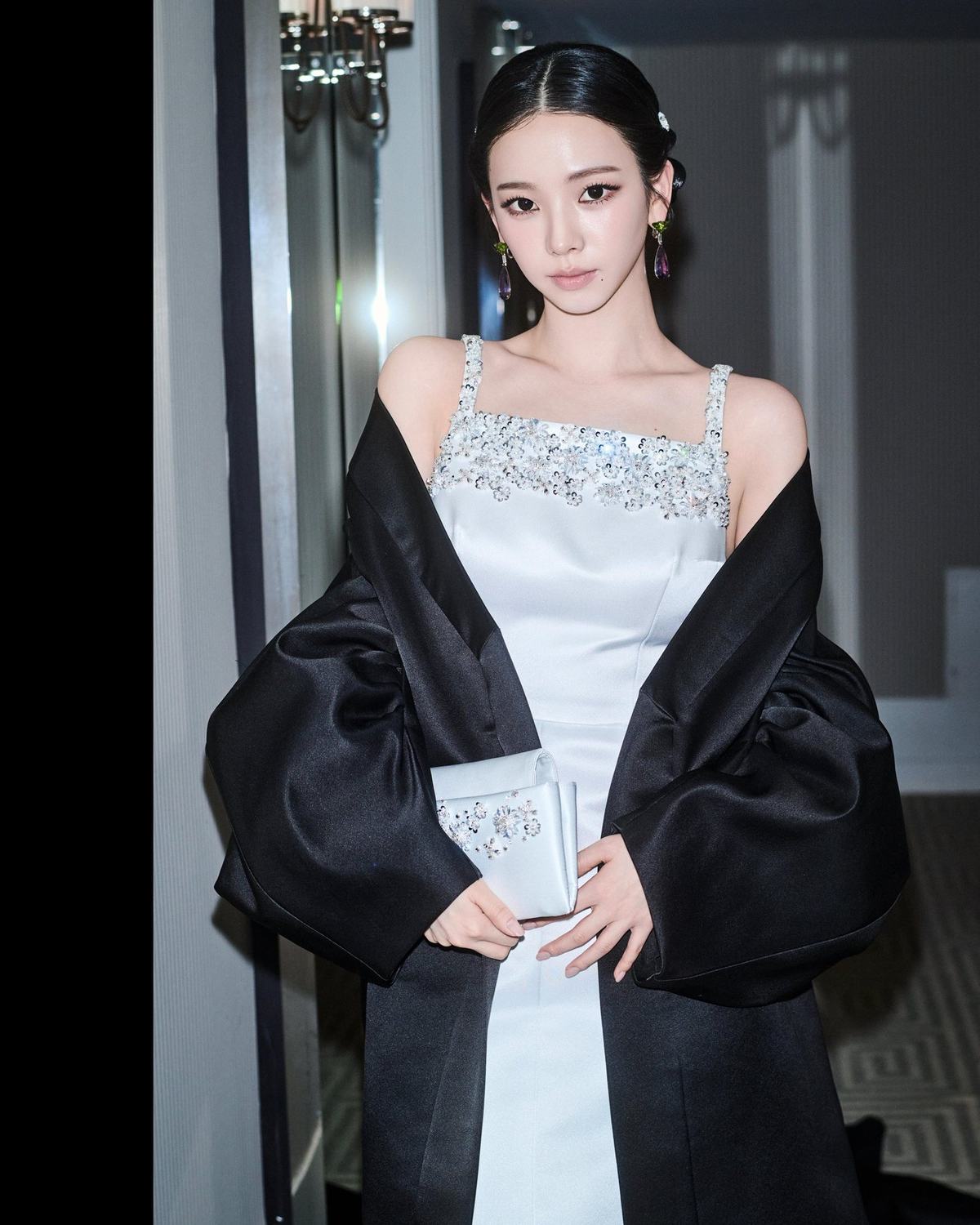 Flash portrait of Karina holding a white clutch with a black cape