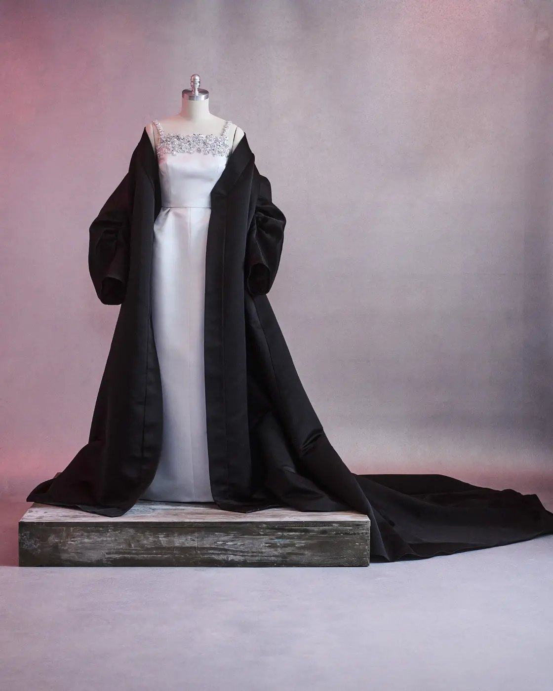 White gown and black cape displayed on a dress form